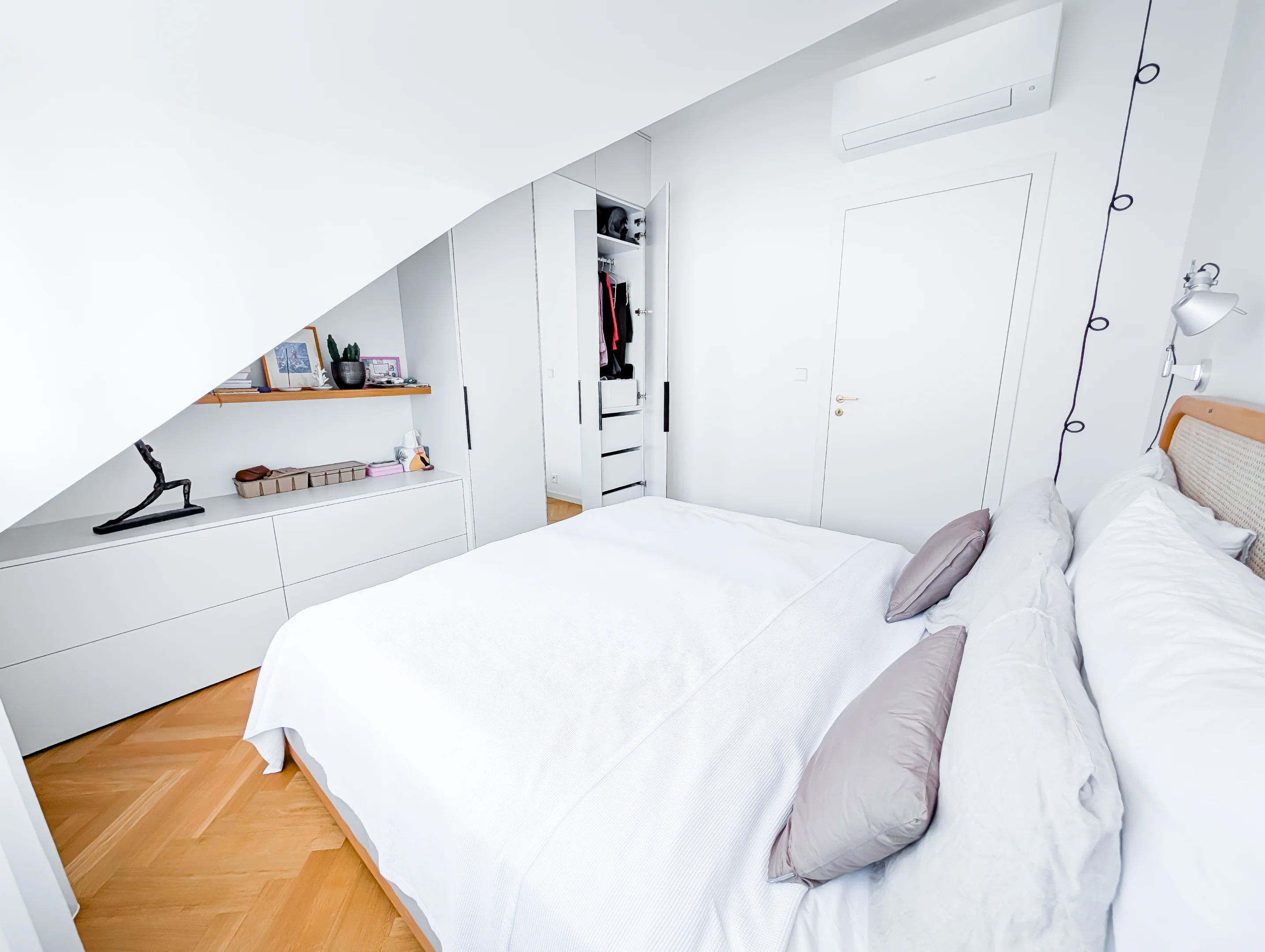 Bílá ložnice s postelí skříní a parketovou podlahou.